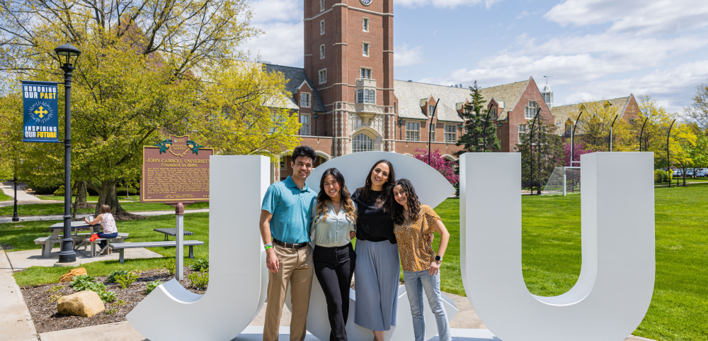 Four students standing close and smiling in front of big letters spelling 